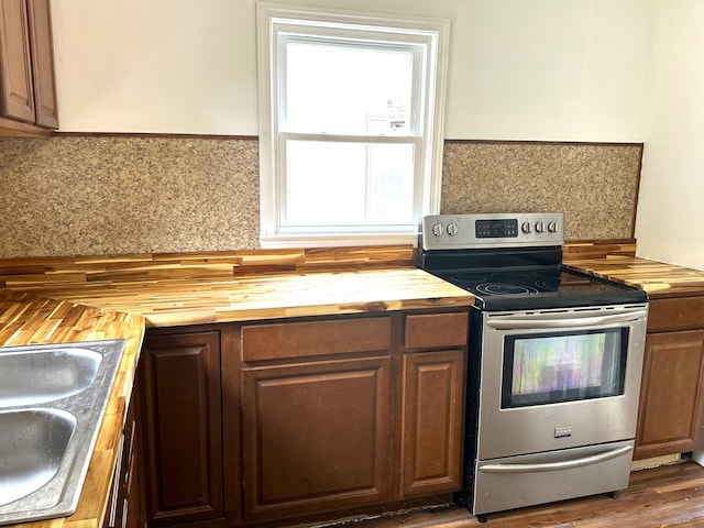 kitchen featuring stainless steel electric range oven, sink, dark hardwood / wood-style flooring, butcher block countertops, and backsplash