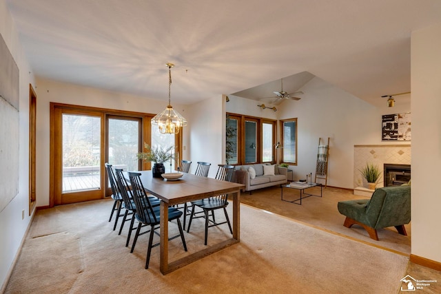 carpeted dining area featuring a tiled fireplace, ceiling fan with notable chandelier, and lofted ceiling