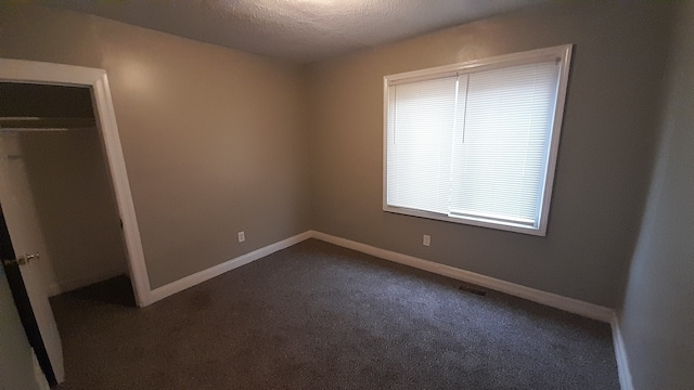 unfurnished bedroom with dark carpet, a textured ceiling, and a closet