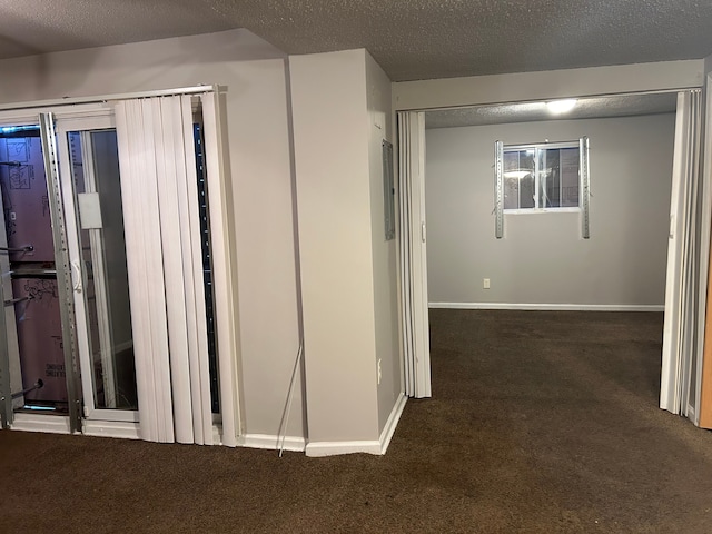 hall featuring dark carpet and a textured ceiling