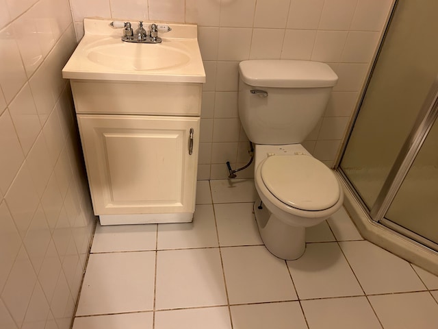 bathroom featuring tile patterned floors, a shower with door, vanity, and tile walls