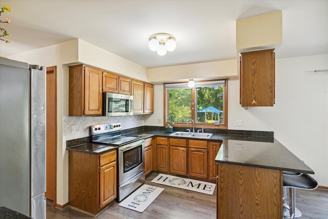 kitchen with sink, kitchen peninsula, a kitchen bar, appliances with stainless steel finishes, and hardwood / wood-style flooring