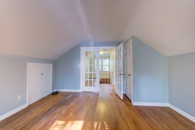 additional living space with french doors, light hardwood / wood-style flooring, and vaulted ceiling