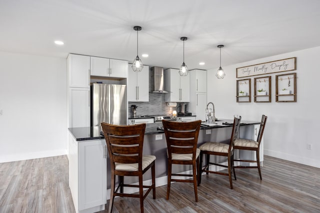 kitchen featuring white cabinetry, decorative light fixtures, stainless steel fridge, decorative backsplash, and wall chimney range hood