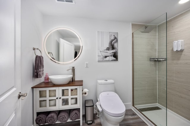 bathroom with hardwood / wood-style flooring, vanity, toilet, and a tile shower