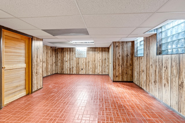 basement featuring a wealth of natural light, a drop ceiling, and wooden walls