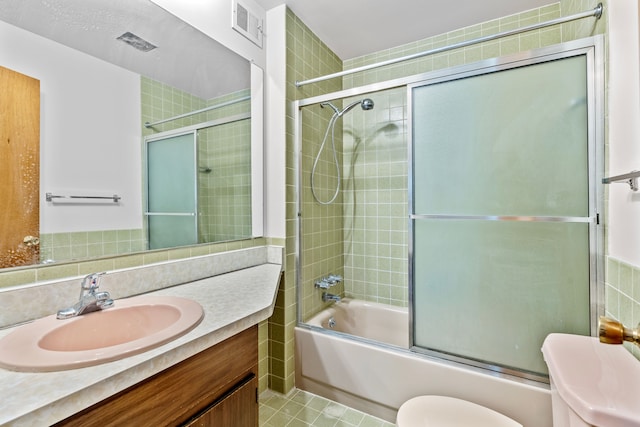 full bathroom featuring tile patterned flooring, bath / shower combo with glass door, toilet, vanity, and tile walls