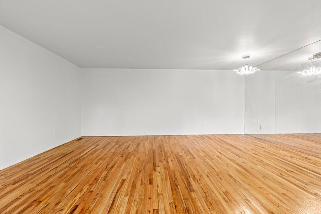 empty room with light hardwood / wood-style floors and a chandelier