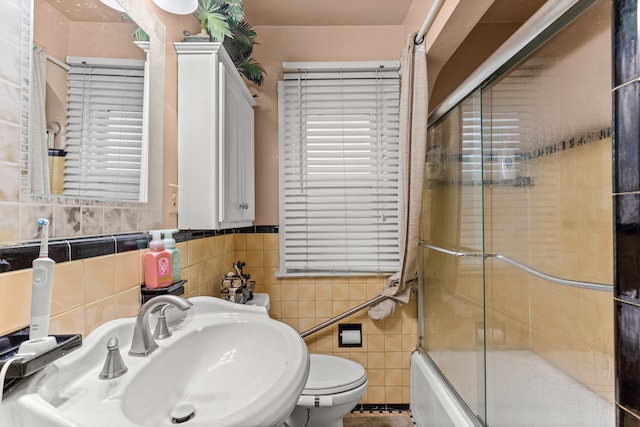 full bathroom with sink, bath / shower combo with glass door, tile walls, and toilet