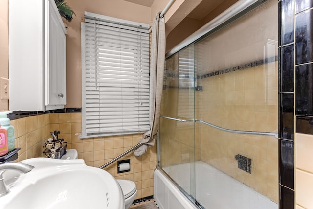 full bathroom featuring bath / shower combo with glass door, toilet, tile walls, and sink