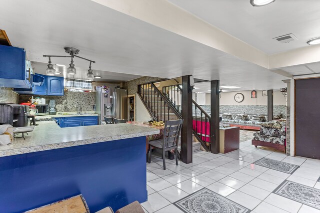 kitchen featuring blue cabinetry, hanging light fixtures, stainless steel fridge with ice dispenser, kitchen peninsula, and light tile patterned flooring