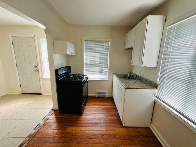 kitchen with black gas stove, white cabinetry, dark wood-type flooring, and sink