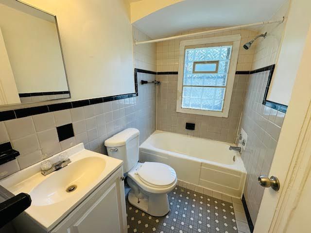 full bathroom featuring tile patterned floors, vanity, tiled shower / bath combo, tile walls, and toilet