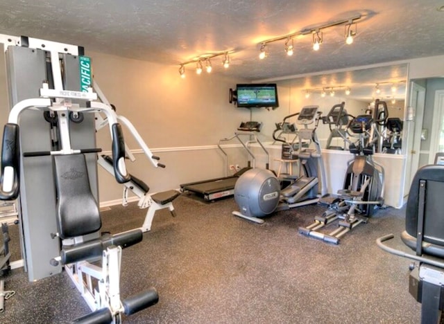 exercise room featuring rail lighting and a textured ceiling