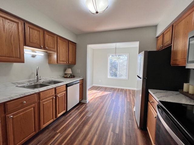 kitchen with dark wood-type flooring, sink, light stone countertops, decorative light fixtures, and stainless steel appliances