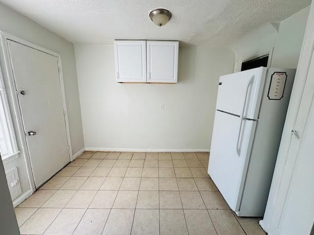 kitchen featuring white cabinets, white fridge, light tile patterned flooring, and a textured ceiling