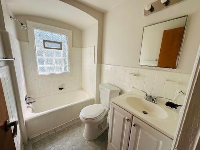 full bathroom featuring tile patterned flooring, toilet, vanity, tile walls, and tiled shower / bath