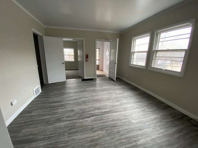 empty room featuring dark hardwood / wood-style floors, ornamental molding, and a wealth of natural light