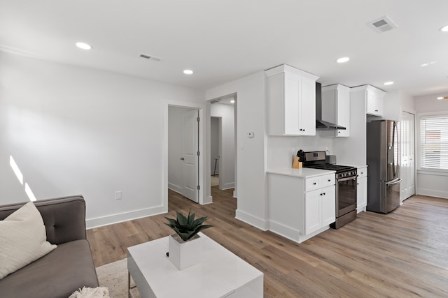 kitchen featuring white cabinetry, light wood-type flooring, appliances with stainless steel finishes, and wall chimney range hood