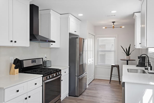 kitchen with wall chimney range hood, sink, light hardwood / wood-style floors, white cabinetry, and stainless steel appliances