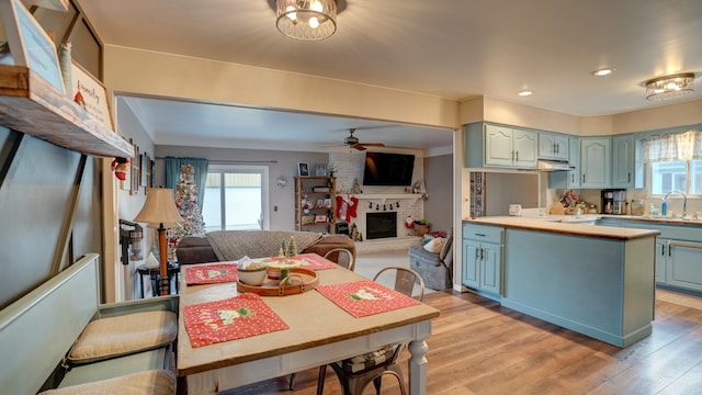 dining space featuring ceiling fan, sink, light hardwood / wood-style floors, and a brick fireplace