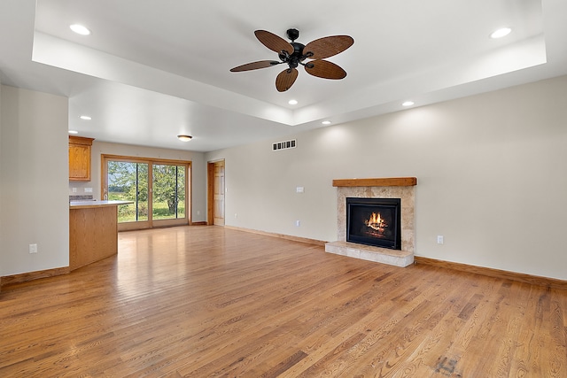 unfurnished living room featuring light hardwood / wood-style floors, a raised ceiling, ceiling fan, and a premium fireplace