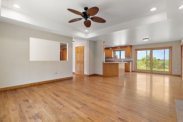 unfurnished living room with ceiling fan, a raised ceiling, light wood-type flooring, and sink