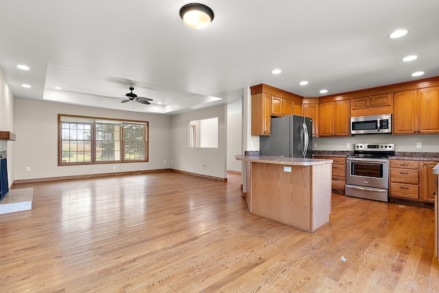 kitchen with ceiling fan, a kitchen breakfast bar, a tray ceiling, appliances with stainless steel finishes, and light wood-type flooring