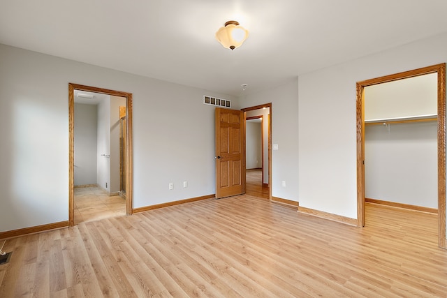 unfurnished bedroom featuring a walk in closet, light hardwood / wood-style flooring, a closet, and connected bathroom