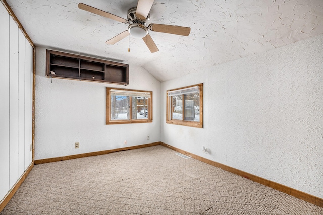 carpeted spare room featuring a textured ceiling, ceiling fan, and lofted ceiling