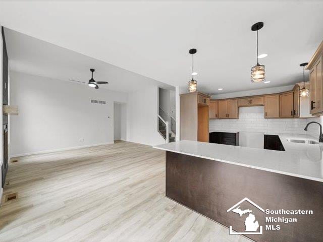 kitchen with tasteful backsplash, sink, decorative light fixtures, and light hardwood / wood-style flooring