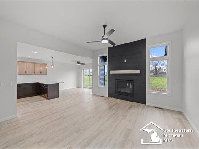 unfurnished living room with ceiling fan, a large fireplace, and light wood-type flooring