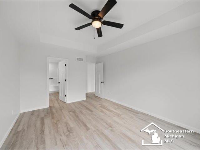 unfurnished bedroom with a tray ceiling, ceiling fan, and light hardwood / wood-style flooring