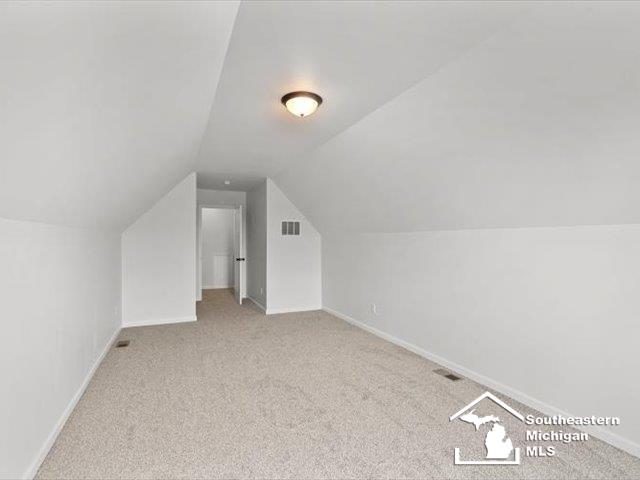 additional living space featuring light colored carpet and lofted ceiling