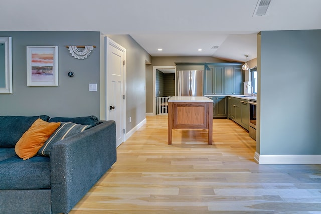 kitchen featuring sink, hanging light fixtures, stainless steel fridge, lofted ceiling, and light wood-type flooring