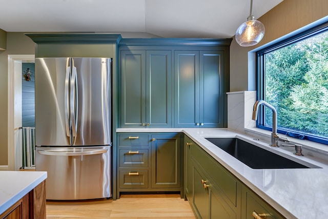 kitchen with lofted ceiling, sink, decorative light fixtures, light hardwood / wood-style floors, and stainless steel refrigerator