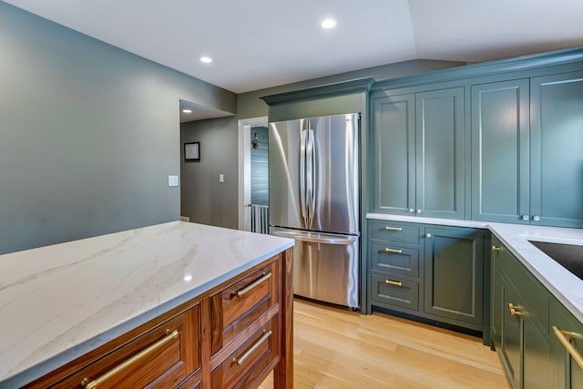 kitchen with stainless steel fridge, light stone counters, lofted ceiling, and light wood-type flooring