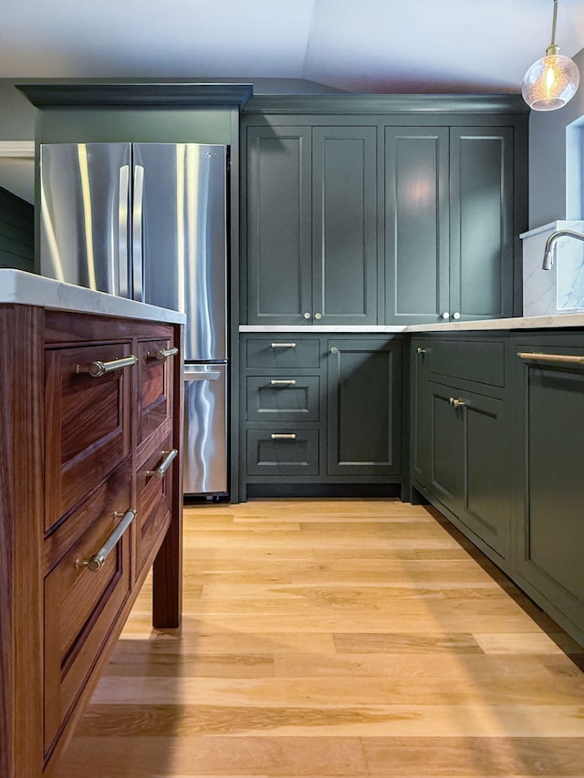 kitchen featuring pendant lighting, light hardwood / wood-style flooring, stainless steel refrigerator, and vaulted ceiling