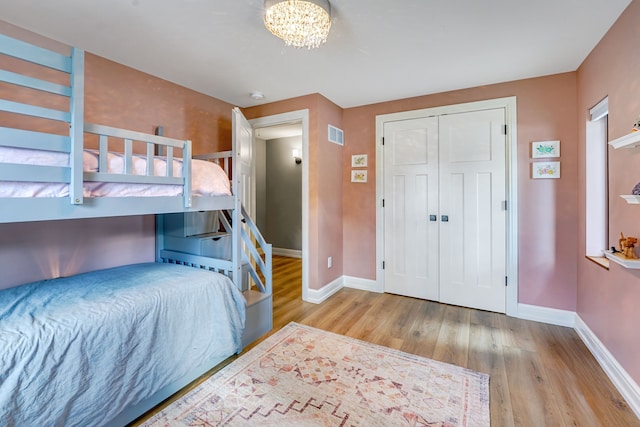 bedroom featuring an inviting chandelier, light wood-type flooring, and a closet