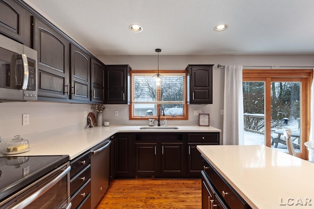 kitchen with appliances with stainless steel finishes, decorative light fixtures, light hardwood / wood-style flooring, and sink