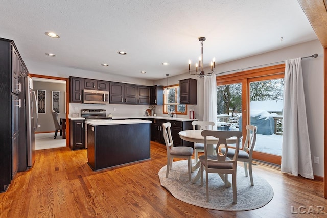 kitchen with pendant lighting, stainless steel appliances, a kitchen island, and light hardwood / wood-style floors