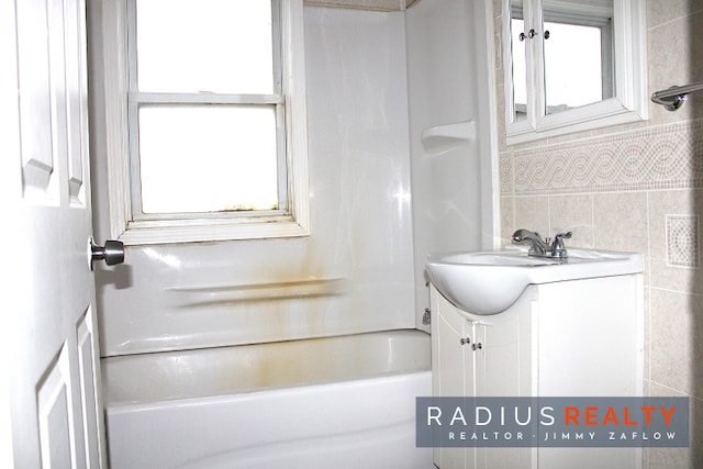 bathroom with bathing tub / shower combination, vanity, and tile walls