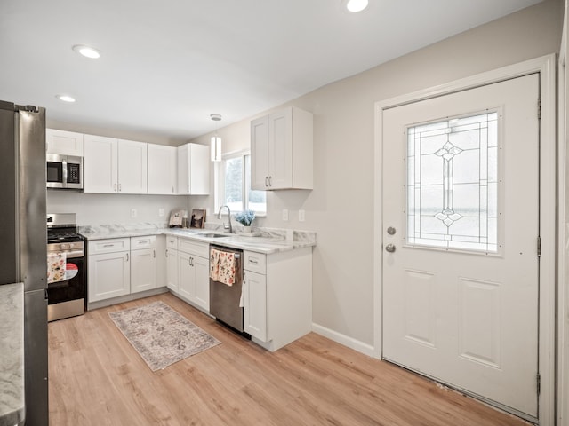 kitchen with sink, hanging light fixtures, light hardwood / wood-style flooring, white cabinets, and appliances with stainless steel finishes