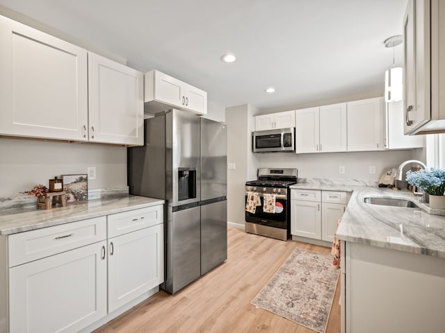 kitchen with white cabinetry, sink, light hardwood / wood-style floors, decorative light fixtures, and appliances with stainless steel finishes