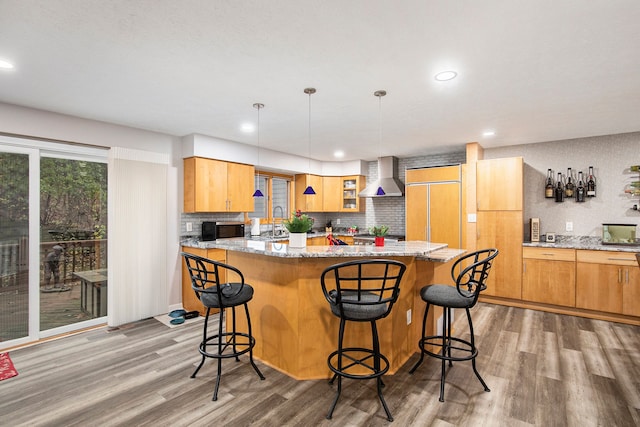 kitchen featuring stainless steel microwave, a kitchen island, wall chimney range hood, light wood-style flooring, and plenty of natural light