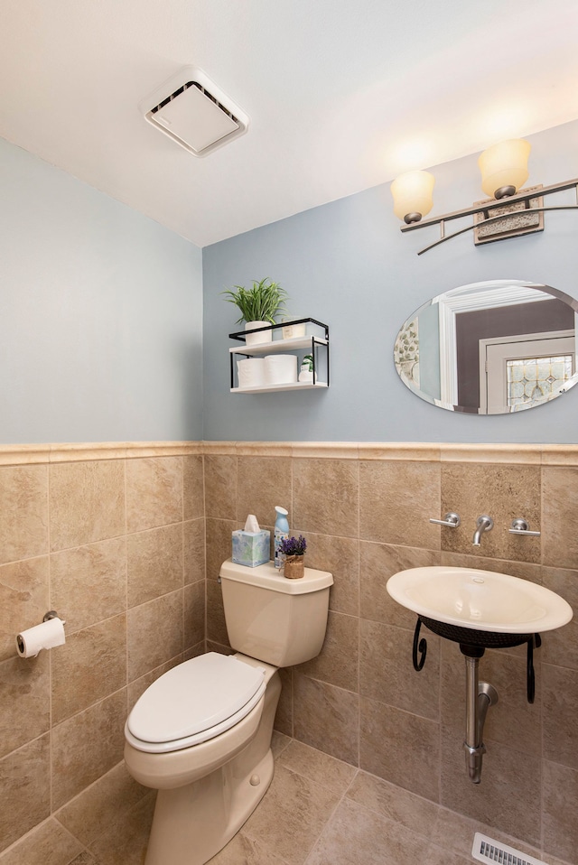 half bathroom with tile patterned floors, a wainscoted wall, toilet, and tile walls