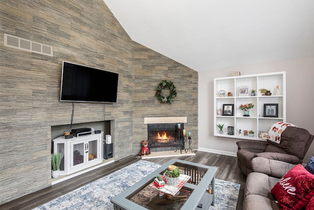 living area featuring visible vents, wood finished floors, a lit fireplace, baseboards, and vaulted ceiling