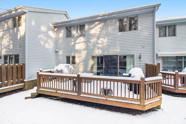 snow covered back of property with a wooden deck and fence