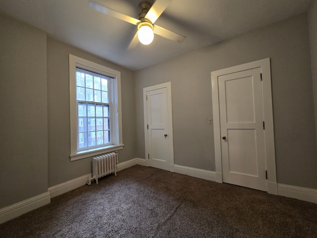 spare room with dark colored carpet, ceiling fan, and radiator heating unit