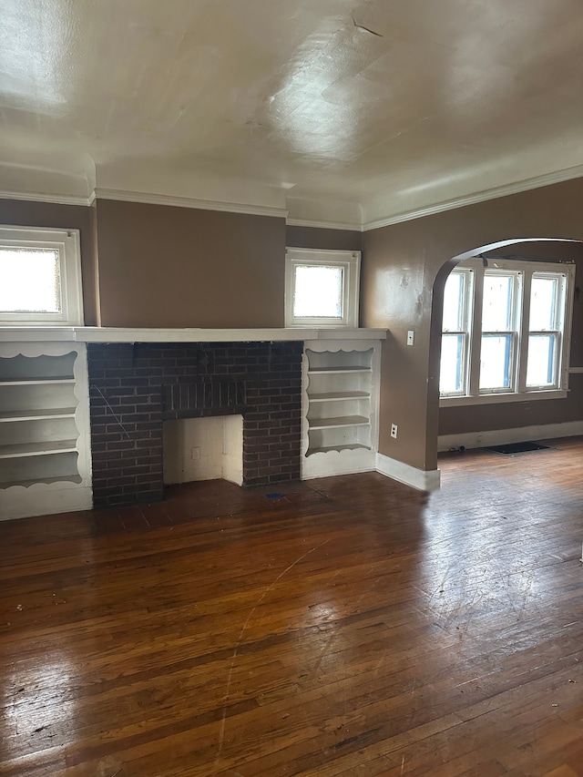 unfurnished living room with dark hardwood / wood-style floors, a brick fireplace, plenty of natural light, and crown molding